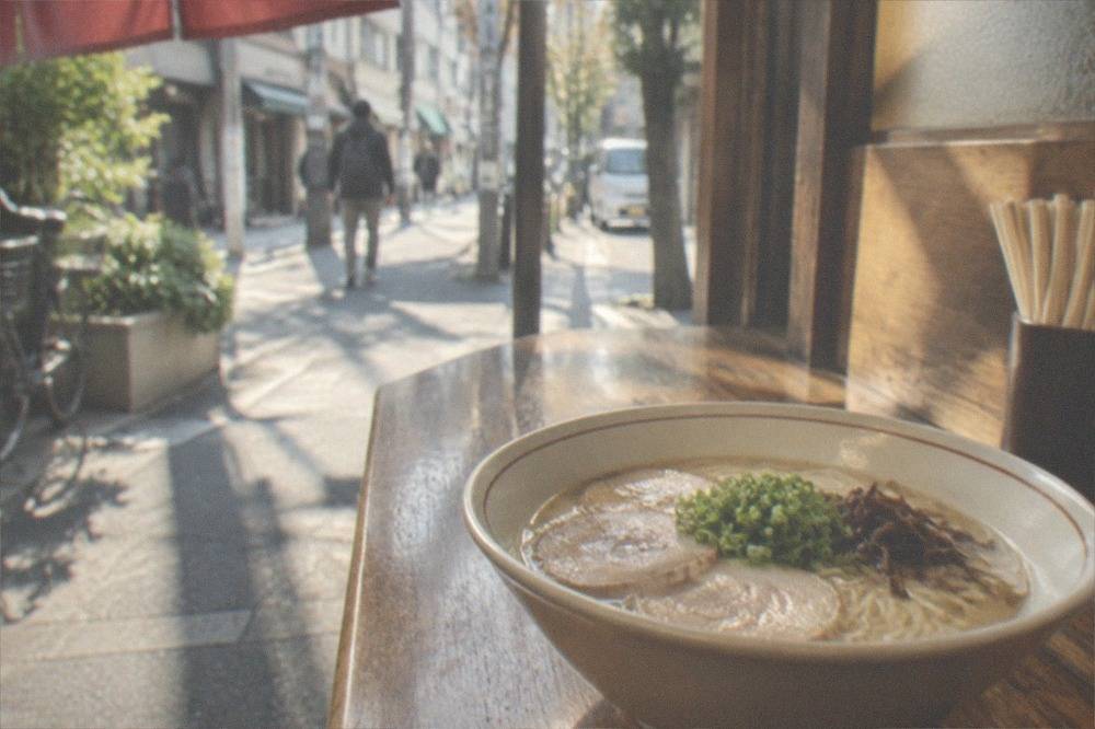 A bowl of ramen with thin noodles and pork slices on a wooden counter