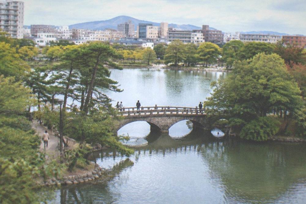 A wide pond with a stone bridge and wooded islands in a city park