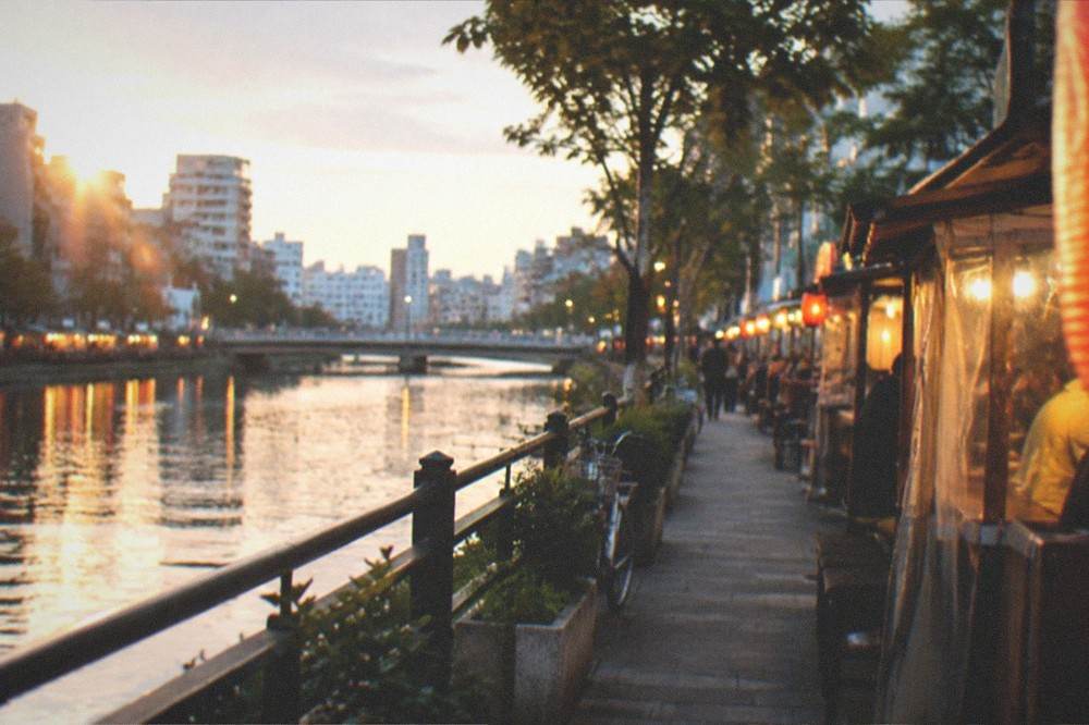 Small lit food stalls reflected in a river at night in Fukuoka