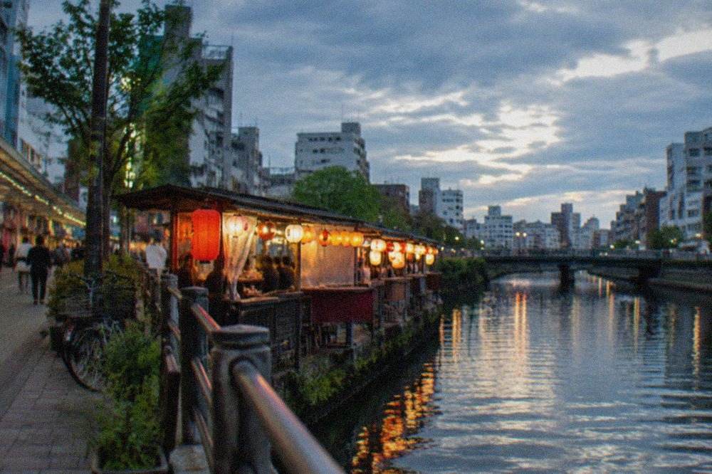 Lanterns glowing over a row of riverside food stalls beside a dark canal at night