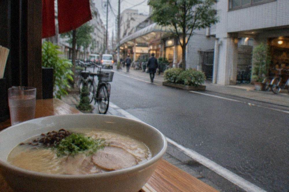 A bowl of white tonkotsu ramen with thin noodles and sliced pork on a wooden counter