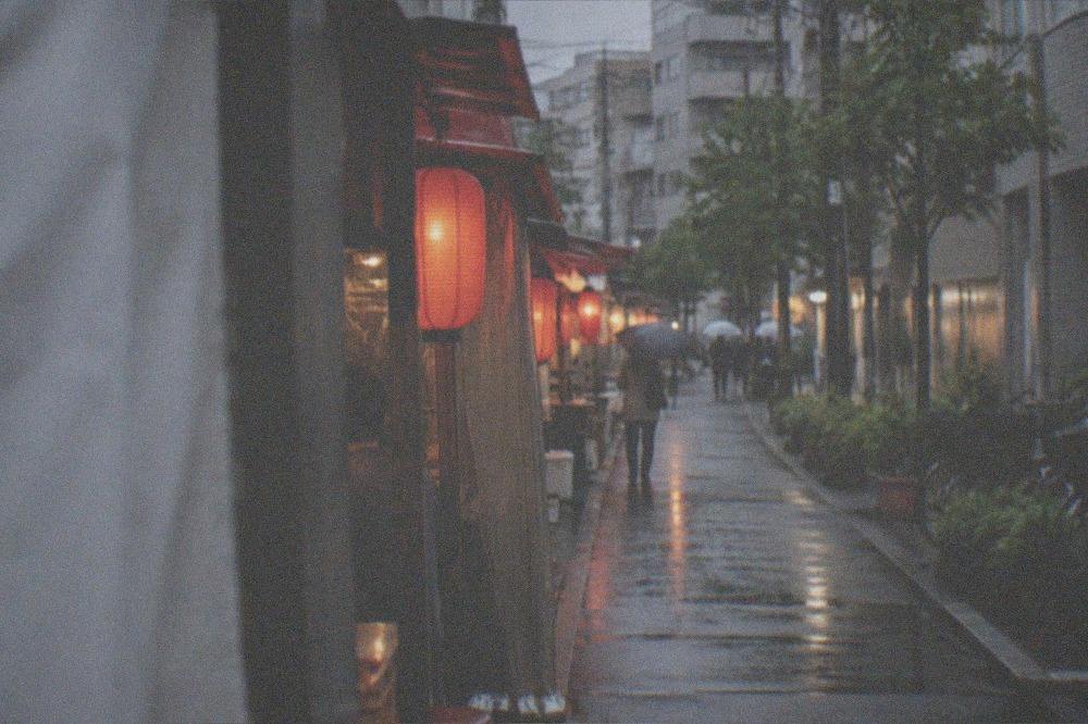 A row of small food stalls with red lanterns lighting a wet evening street