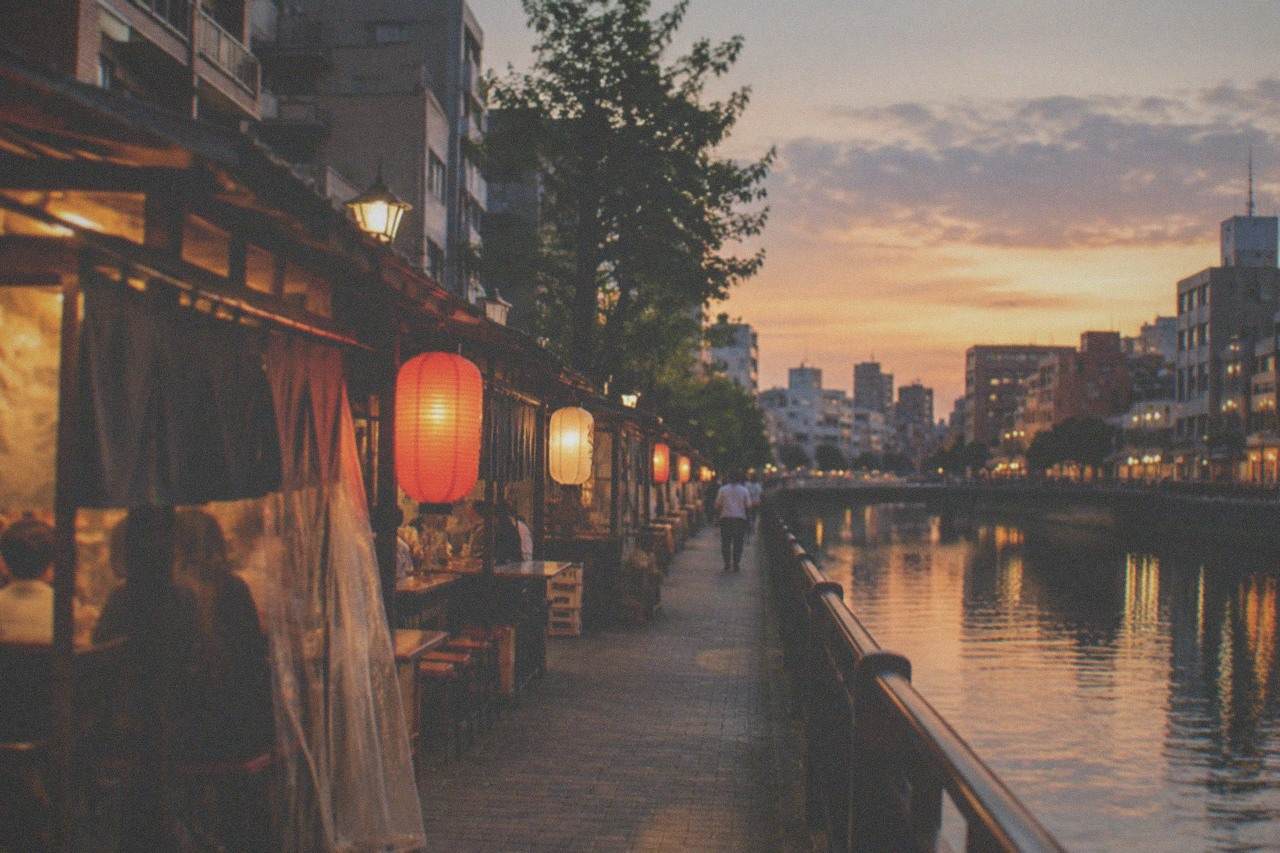 Lanterns glowing over a row of riverside food stalls beside a dark canal at night