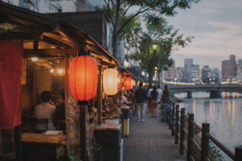 Illuminated food stalls lined along a riverfront street in a Japanese city at night