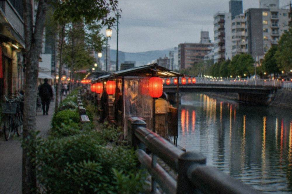 Red paper lanterns glowing outside evening food stalls beside a canal in a Japanese city