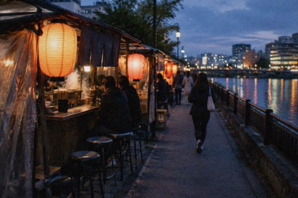 Lantern-lit yatai food stalls lined up along a river at night in a Japanese city