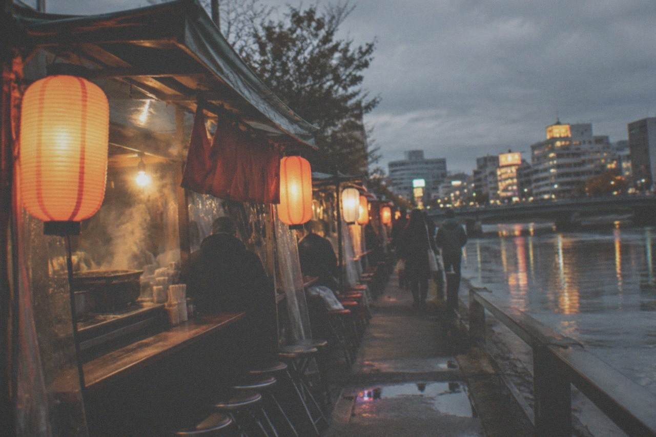 Lantern-lit yatai food stalls lined up along a river at night in a Japanese city