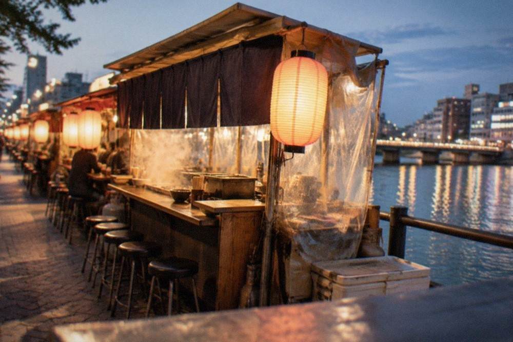 A row of glowing yatai food stalls lining the Naka River at night in the Nakasu district
