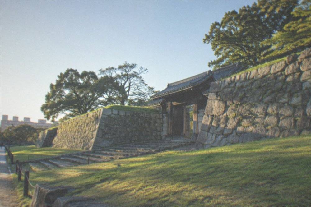 Stone walls of Fukuoka Castle ruins rising above green lawns in Maizuru Park under a clear sky